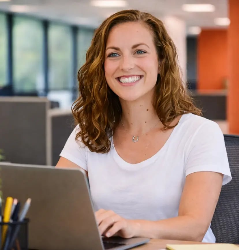 Woman in white shirt smiling and working at laptop