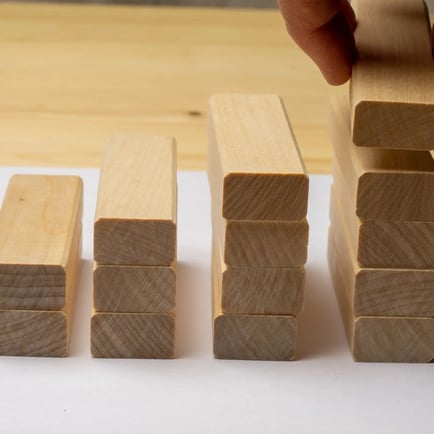 Man putting wooden block on tallest stack of wood block ascending upward