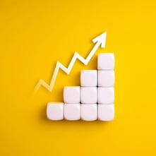 Stack of white blocks in an upward height with an increasing zigzag arrow o n a yellow background