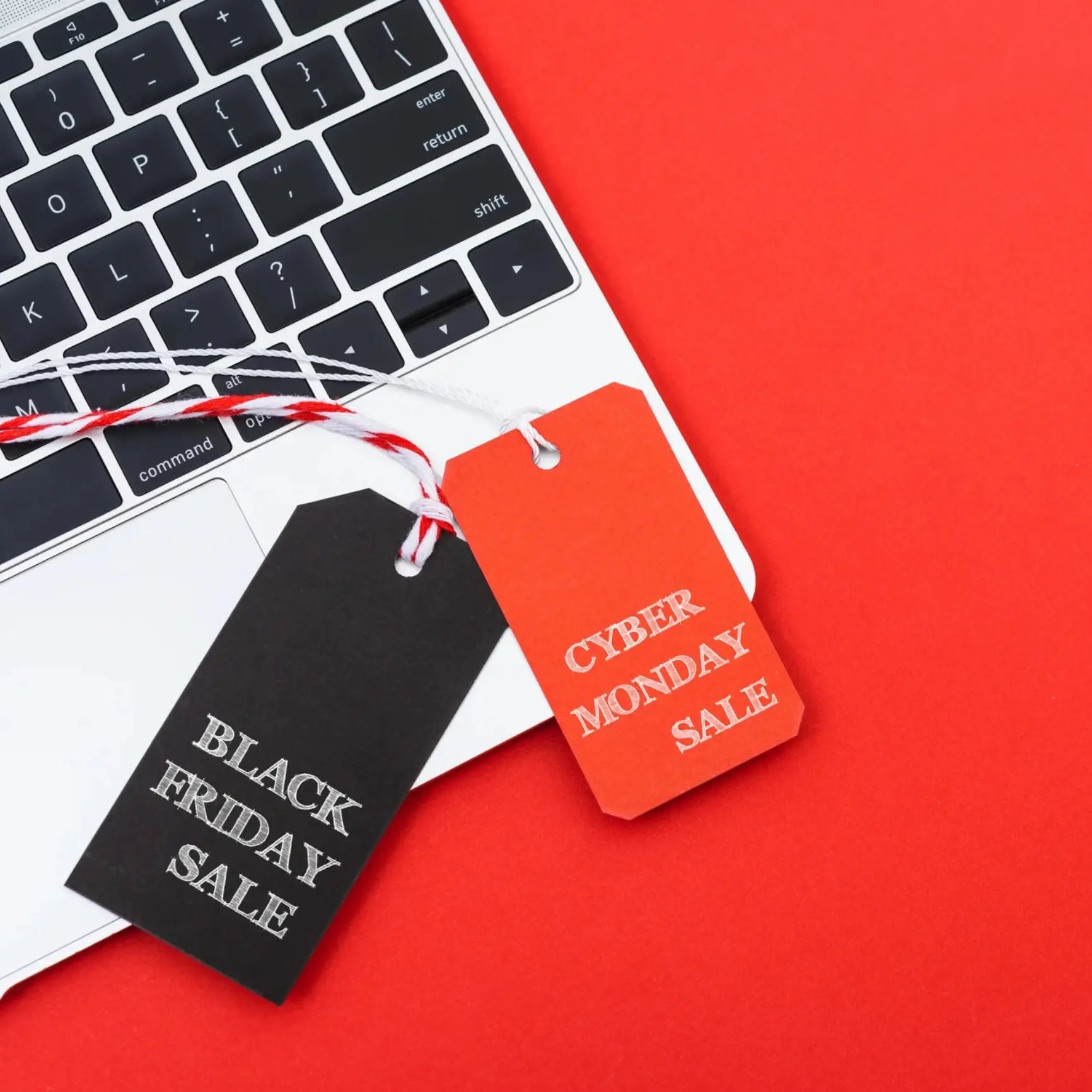 Black Friday and Cyber Monday sale tags on a laptop keyboard, set against a bright red background.