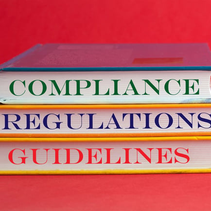 stack of books with the words compliance, regulations and guidelines on thier pages on a red background