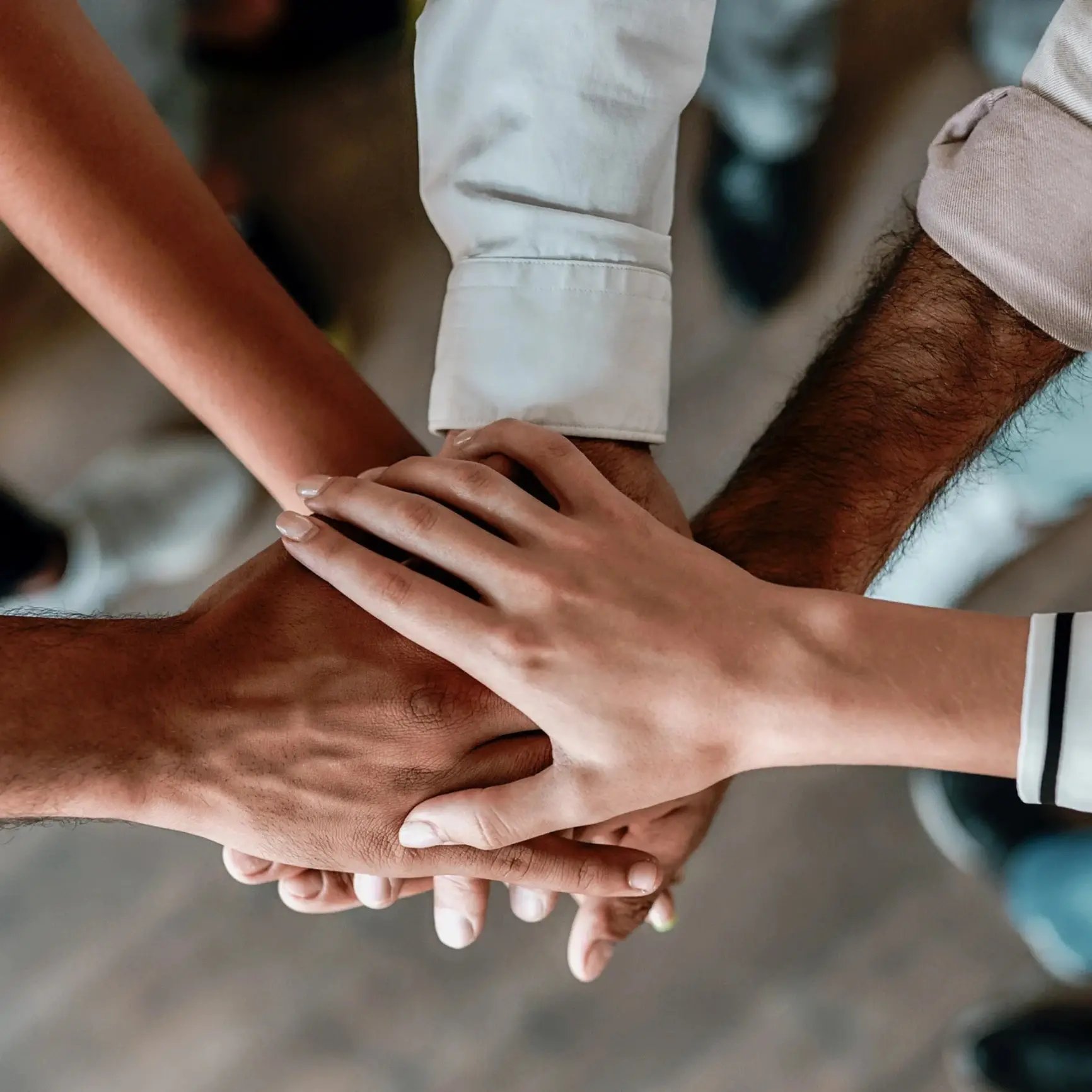 Diverse group of people put hands one on top of the other in an office setting