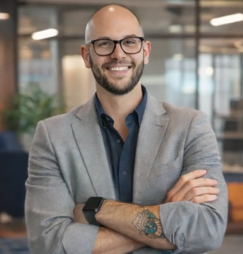 Man in glasses and grey suit standing with arms crossed in an office setting