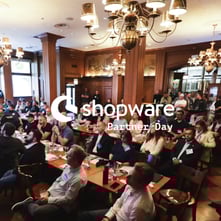Board room filled with executives at Shopware event covered by the white Shopware Partner Day logo