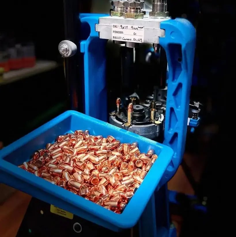 Blue reloading press with tray of copper bullets and brass casings