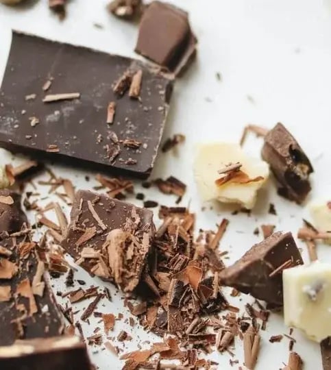 Assorted dark and white chocolate pieces with shavings scattered on a white surface, creating a rich and textured composition
