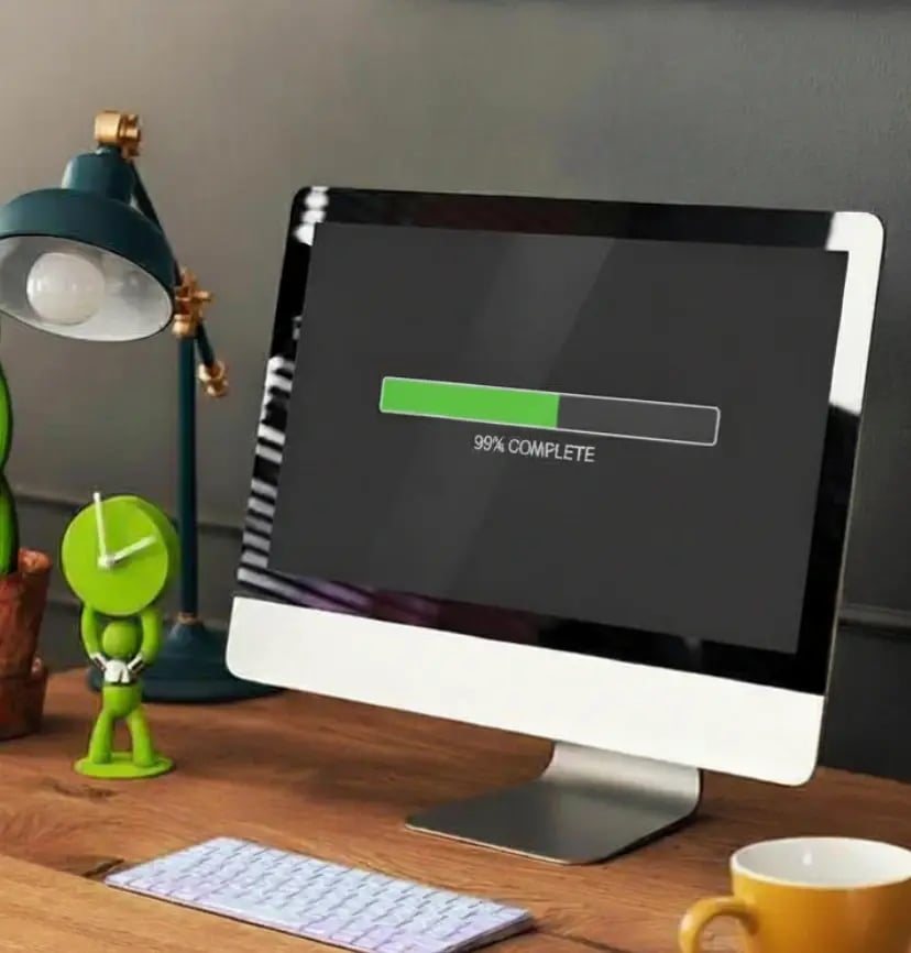 Desktop computer displaying a loading progress bar at 99% completion, representing website performance optimization, fast loading speed, and user experience improvement on a modern workspace