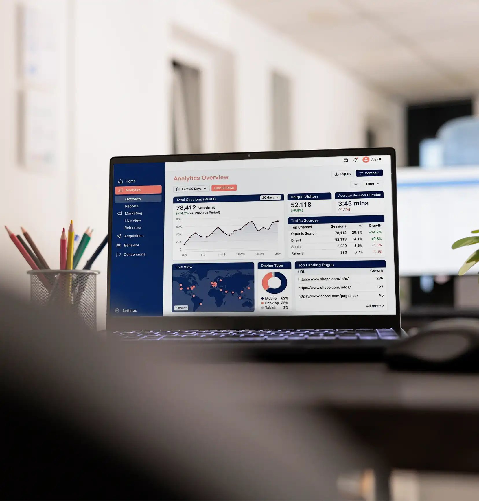 A laptop displaying an analytics dashboard in an office; charts and graphs show website traffic data. A pencil holder sits to the left, conveying productivity