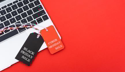 Black Friday and Cyber Monday sale tags on a laptop keyboard, set against a bright red background.